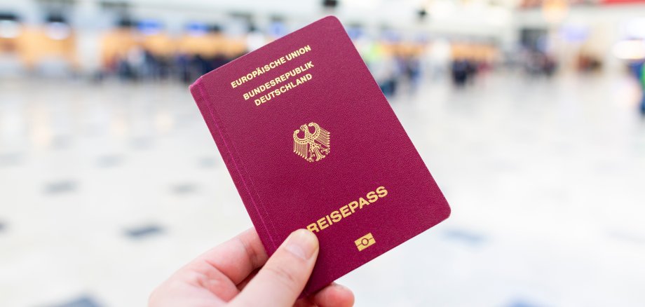 A hand holds a german passport in an airport terminal