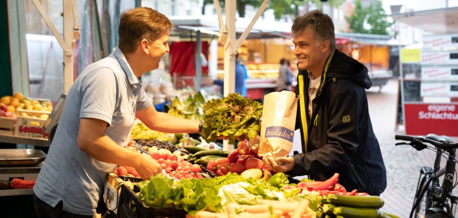Obsthändler übergibt Ware an Kunden auf Wochenmarkt