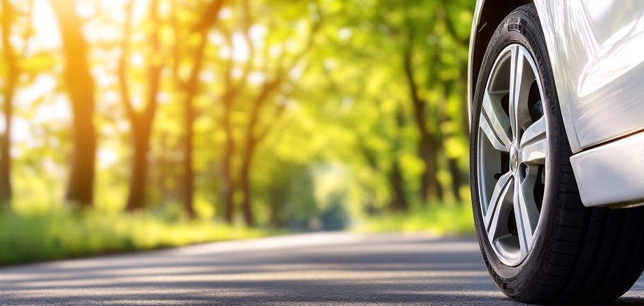 Close up of a car wheel on a serene country road with lush green trees and sunlight : Generative AI
