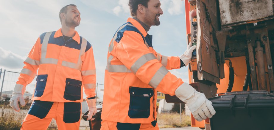 Zwei Müllwerker leeren Mülltonnenbehälter während der Müllabfuhr