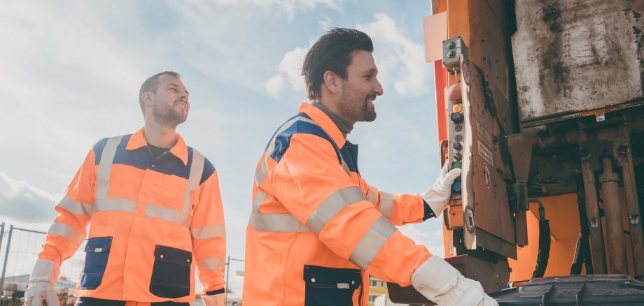 Zwei Müllwerker leeren Mülltonnenbehälter während der Müllabfuhr