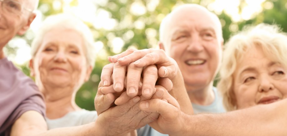 Group of elderly people putting hands together as symbol of unity