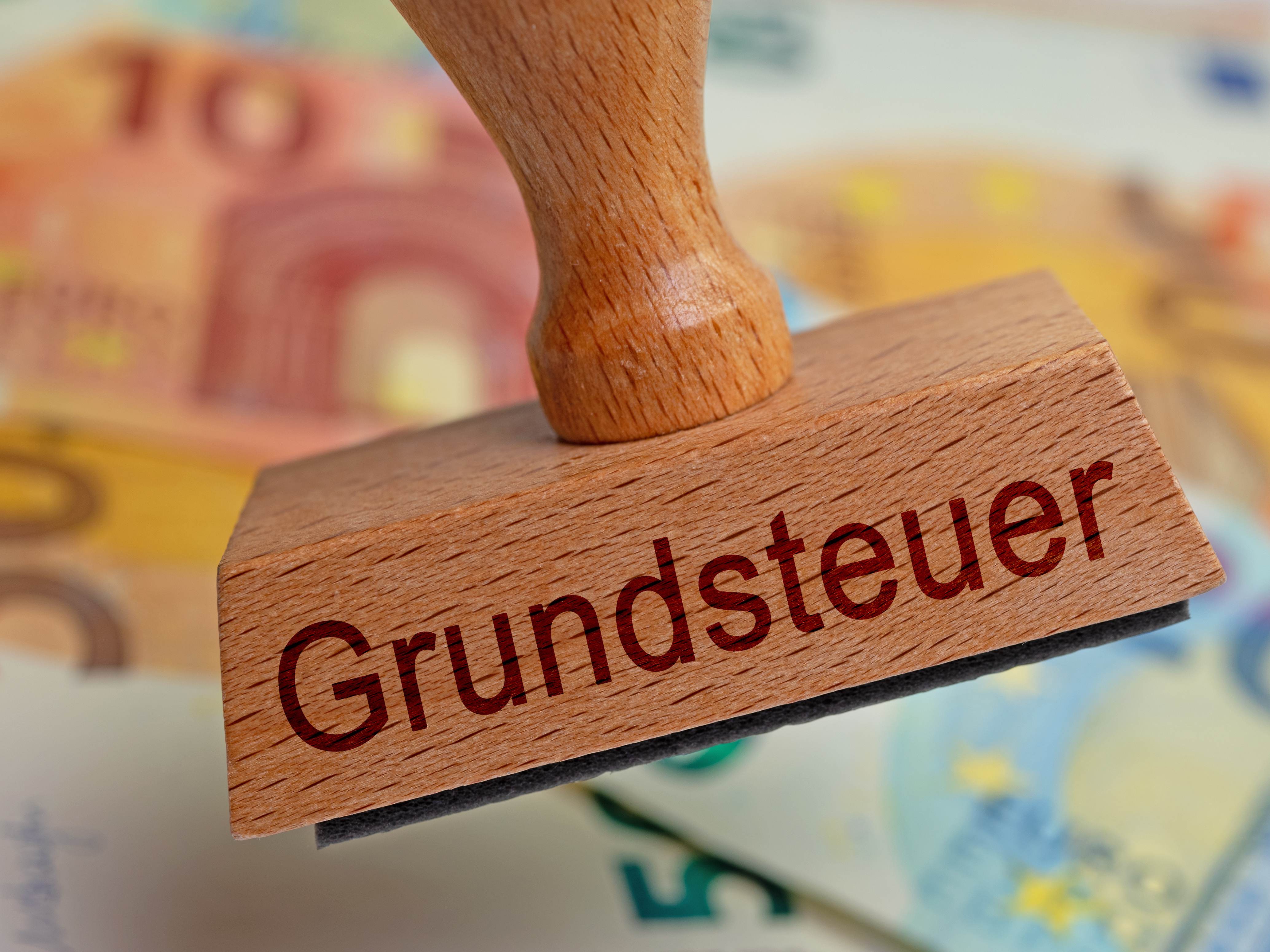 Stempel mit dem Aufdruck "Grundsteuer" vor Geldscheinen