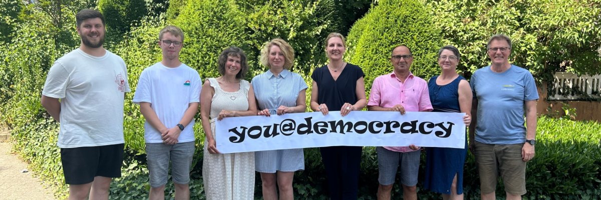 Bürgermeisterin Karin Rodeheger und Projektverantwortliche halten Banner mit der Aufschrift "you@democracy" hoch