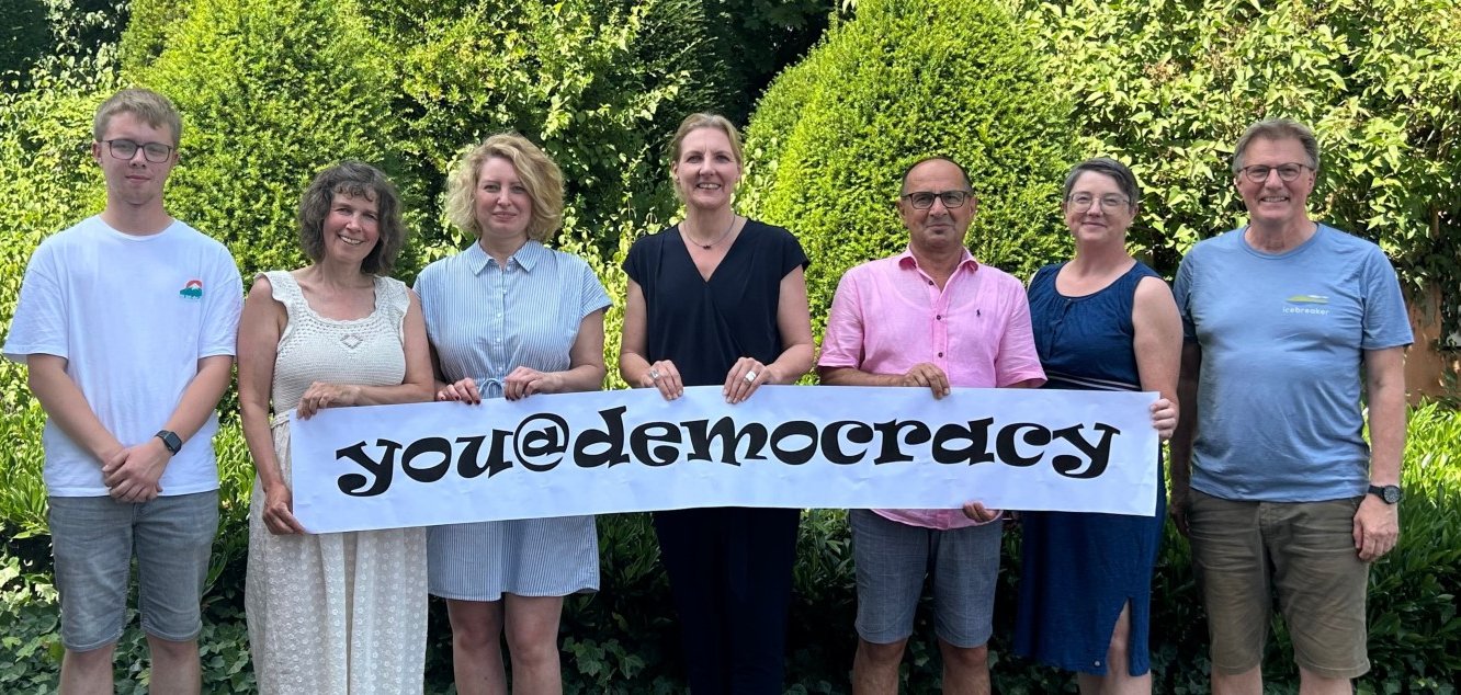 Bürgermeisterin Karin Rodeheger und Projektverantwortliche halten Banner mit der Aufschrift "you@democracy" hoch