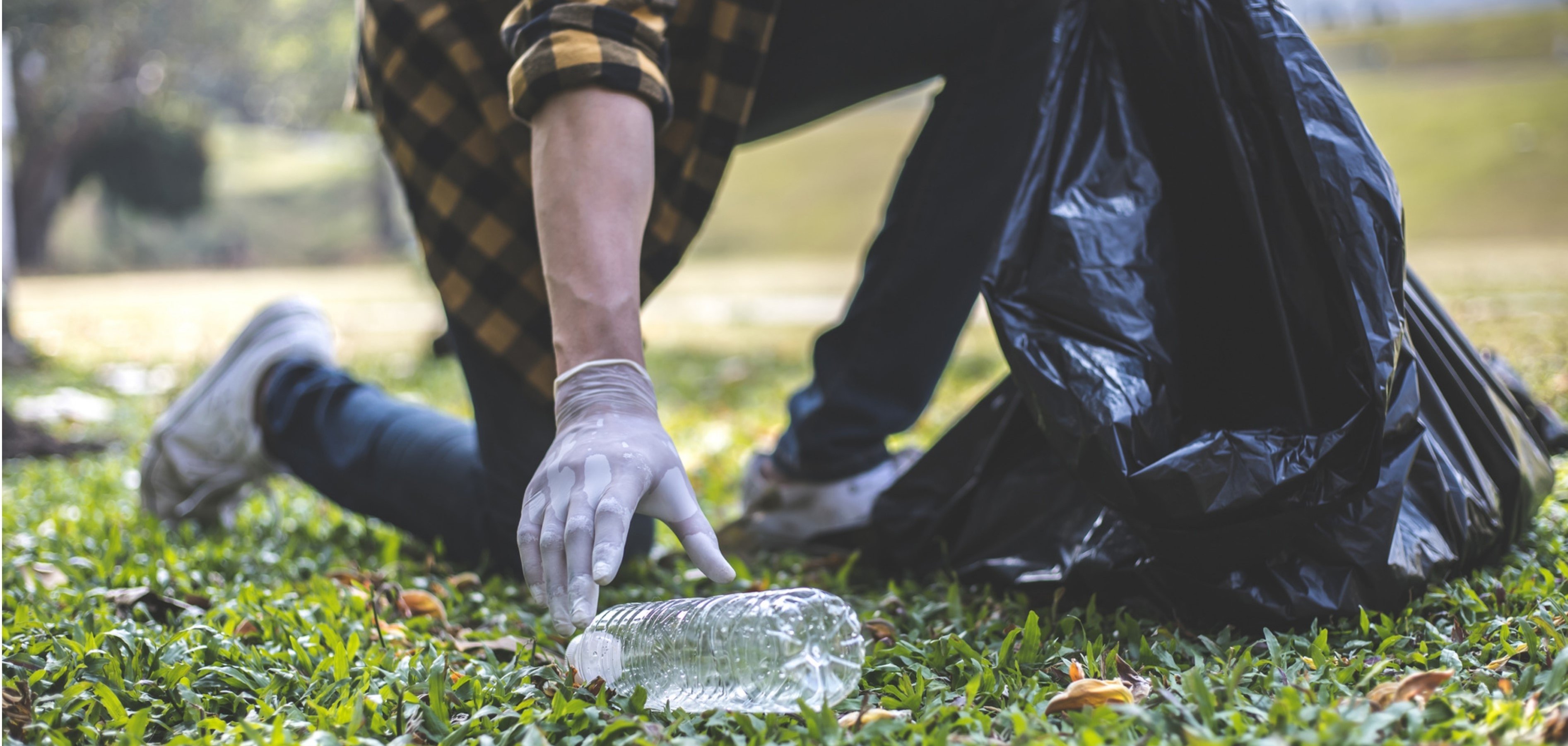 Person sammelt Plastikmüll auf einer Wiese ein
