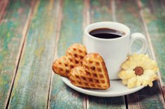 Tasse Kaffee mit Waffelherzen und Blüte