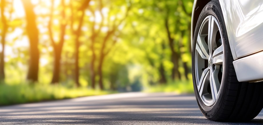 Close up of a car wheel on a serene country road with lush green trees and sunlight : Generative AI