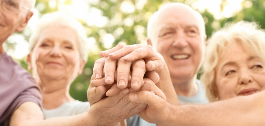 Group of elderly people putting hands together as symbol of unity