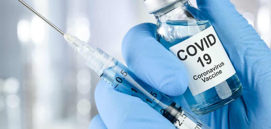 Healthcare cure concept with a hand in blue medical gloves holding Coronavirus, Covid 19 virus, vaccine vial