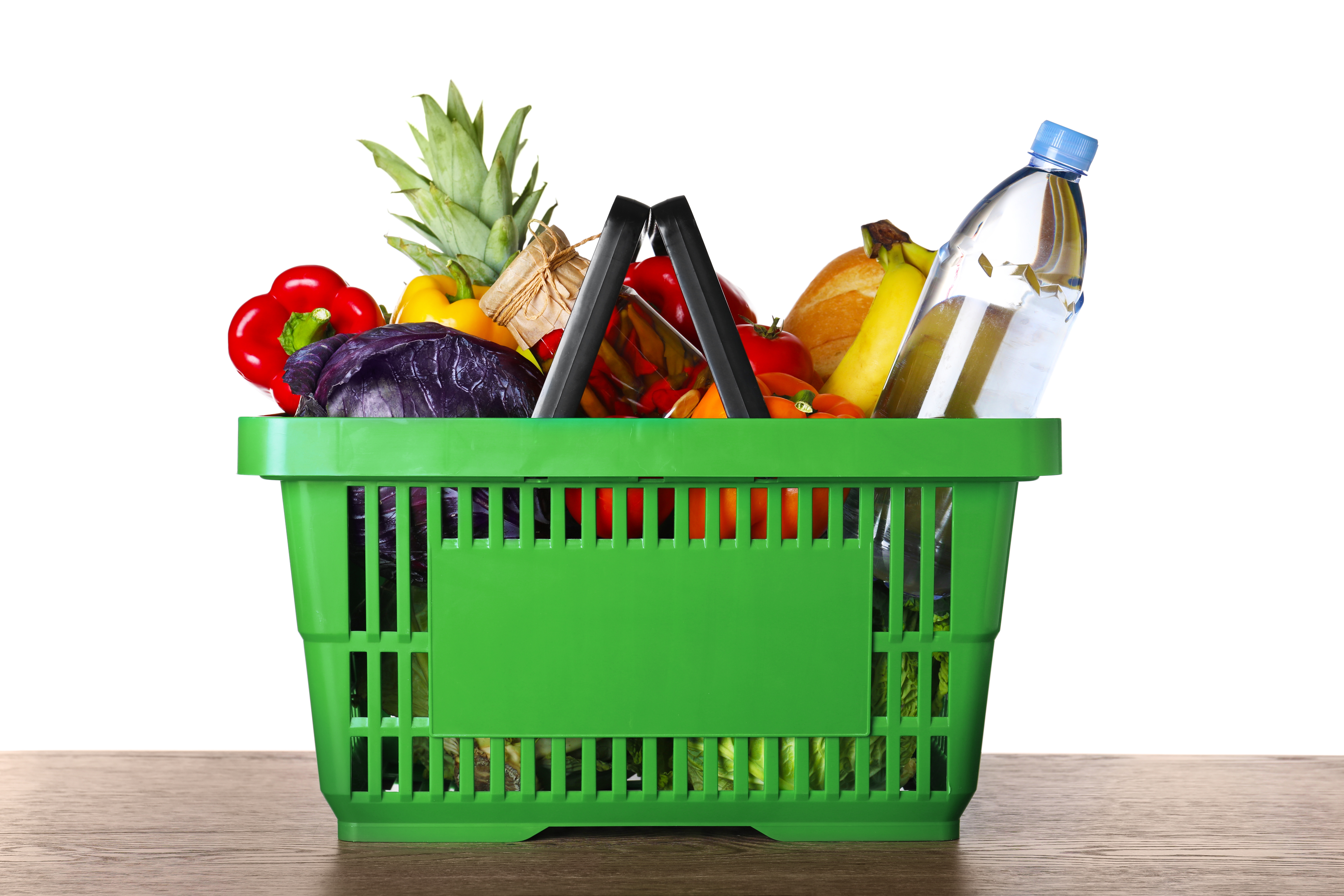 Shopping basket with grocery products on wooden table against white background