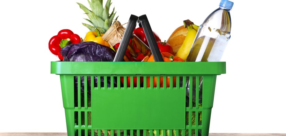 Shopping basket with grocery products on wooden table against white background